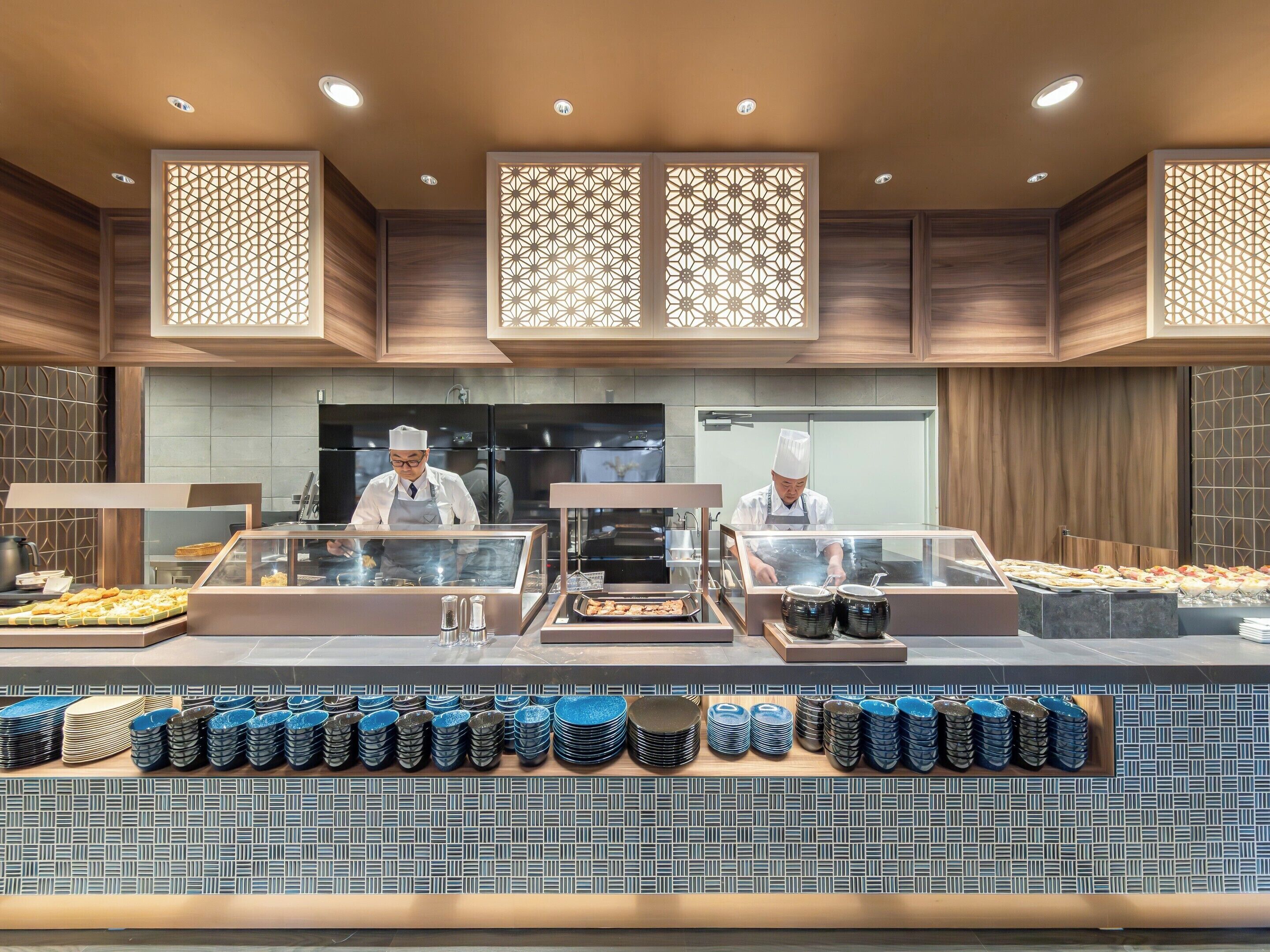 A buffet area with chefs preparing food, a variety of dishes displayed, and a patterned tile backsplash.