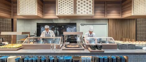 A buffet area with chefs preparing food, a variety of dishes displayed, and a patterned tile backsplash.