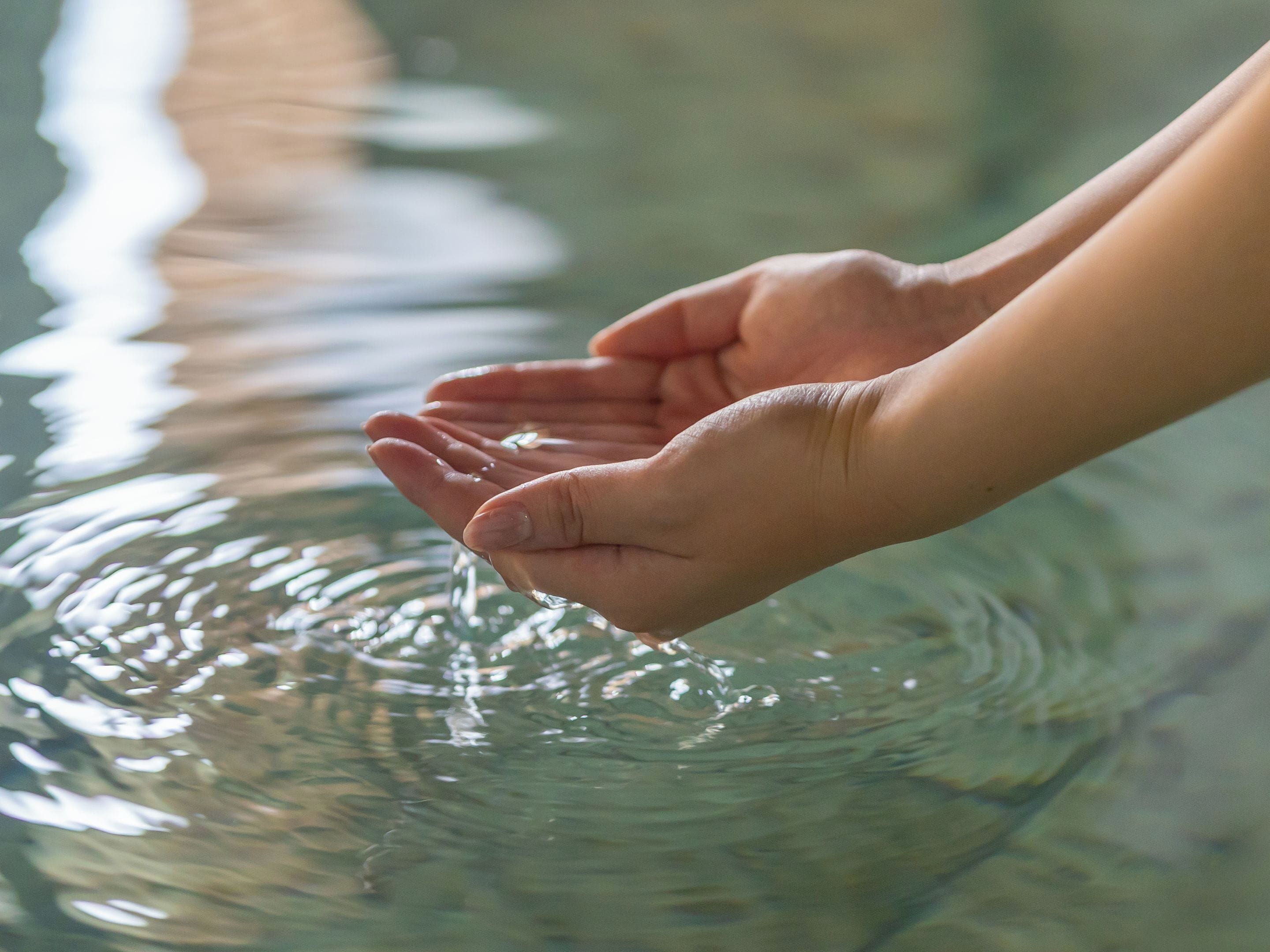 A pair of hands cupped over a body of water, creating ripples.