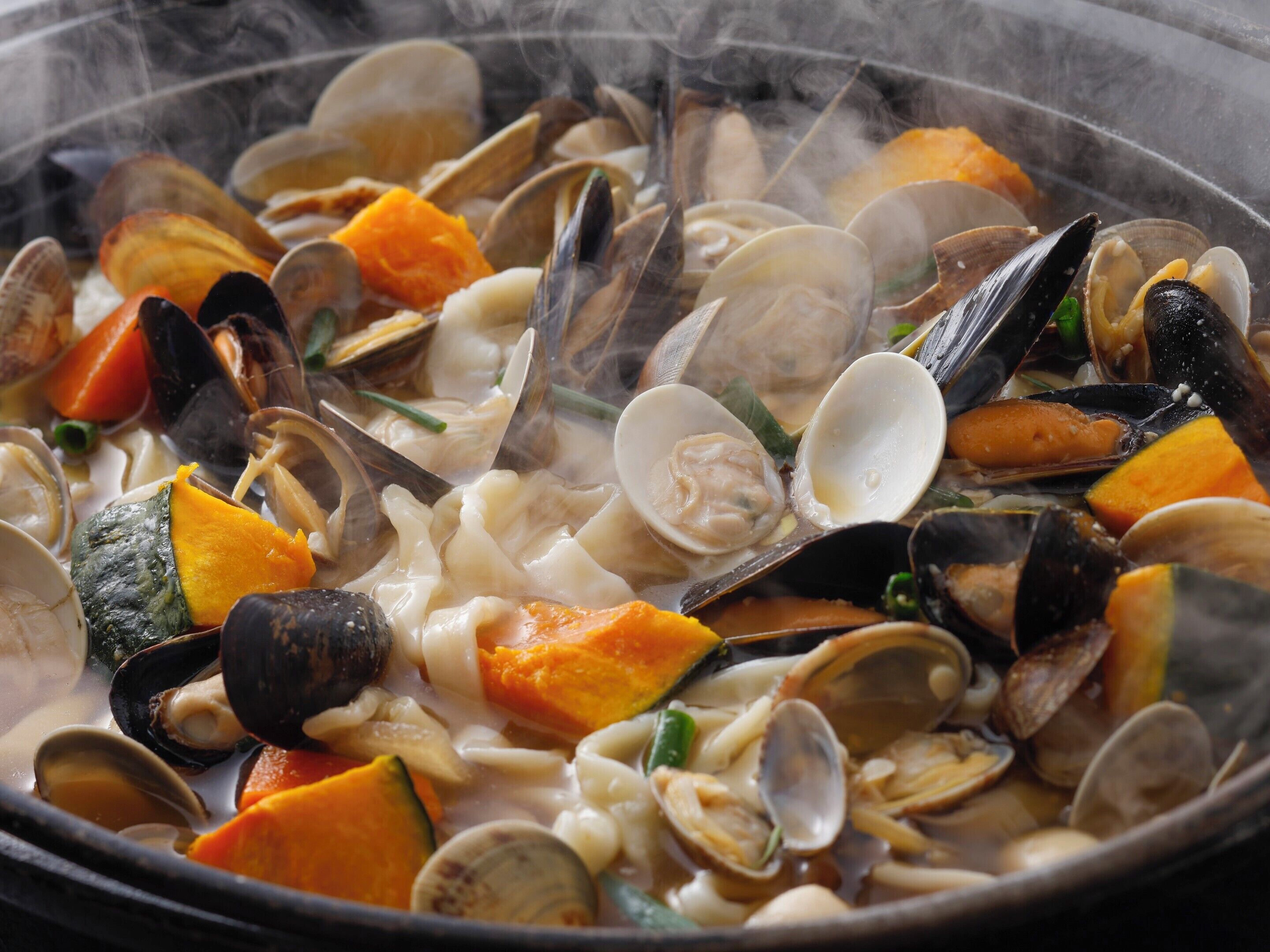 A close-up of a seafood dish with clams, mussels, and vegetables in a pot.