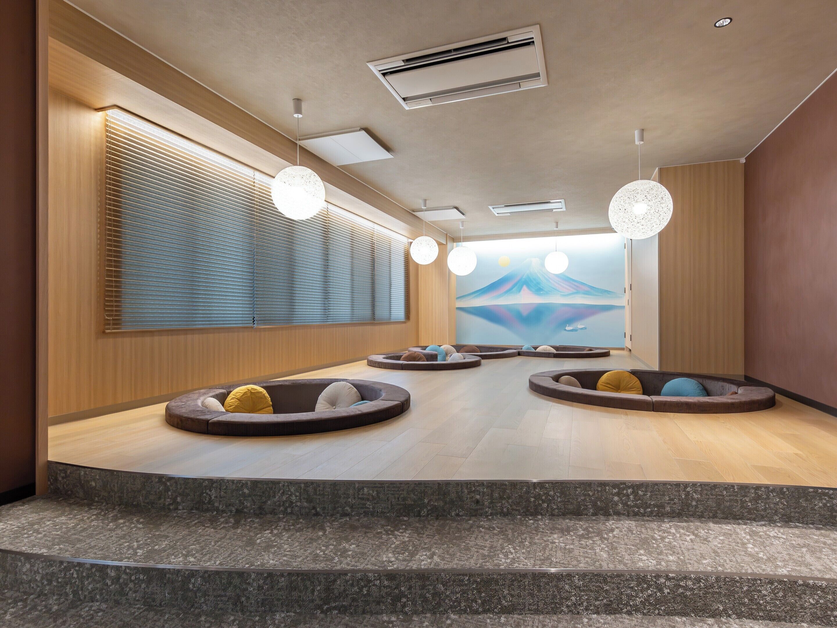 A modern interior with a central seating area, a large window with blinds, and a wall-mounted air conditioning unit.