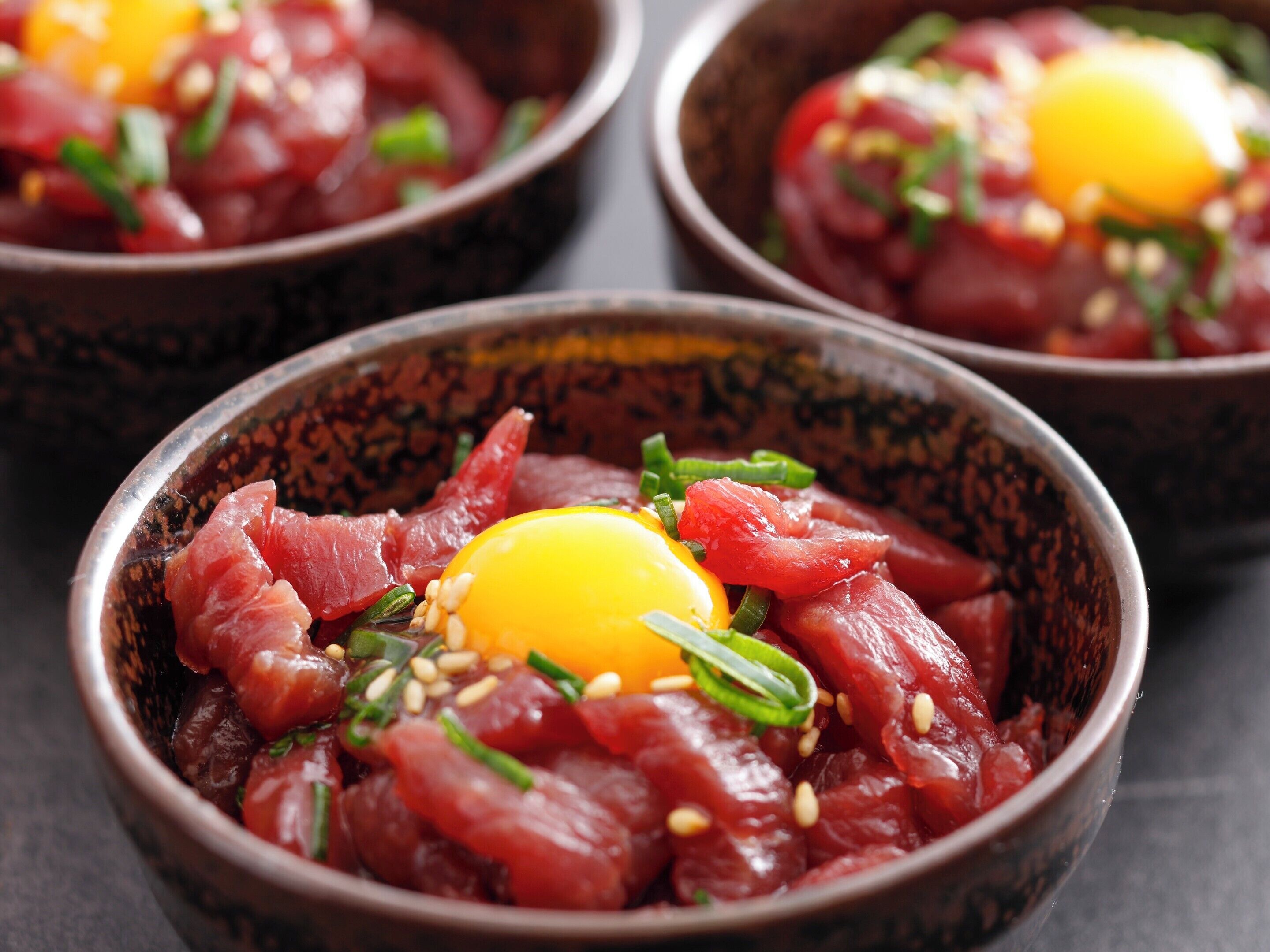 A close-up of a dish with raw fish, an egg, and green onions.
