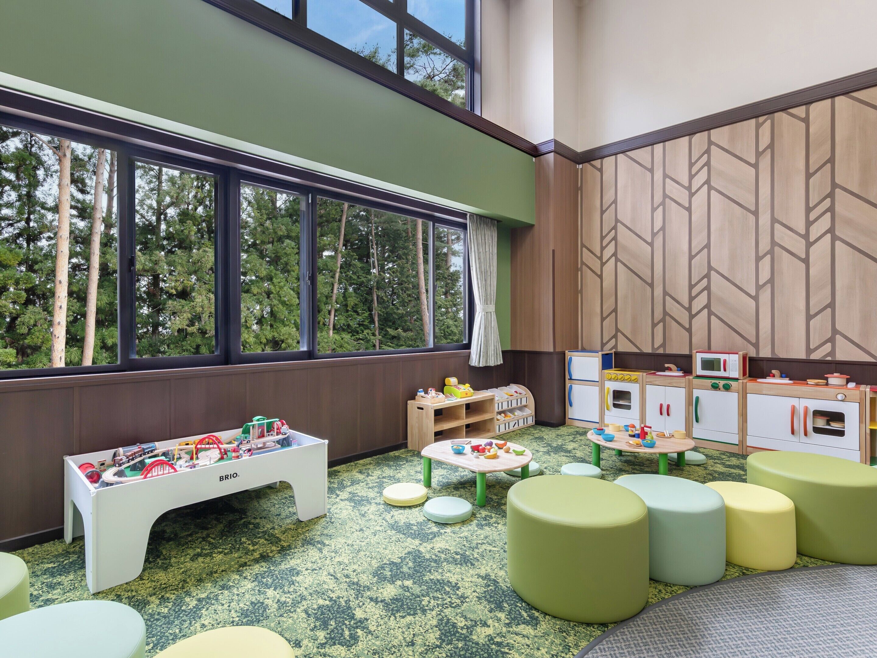 A children's playroom with a large window, play tables, and storage units.