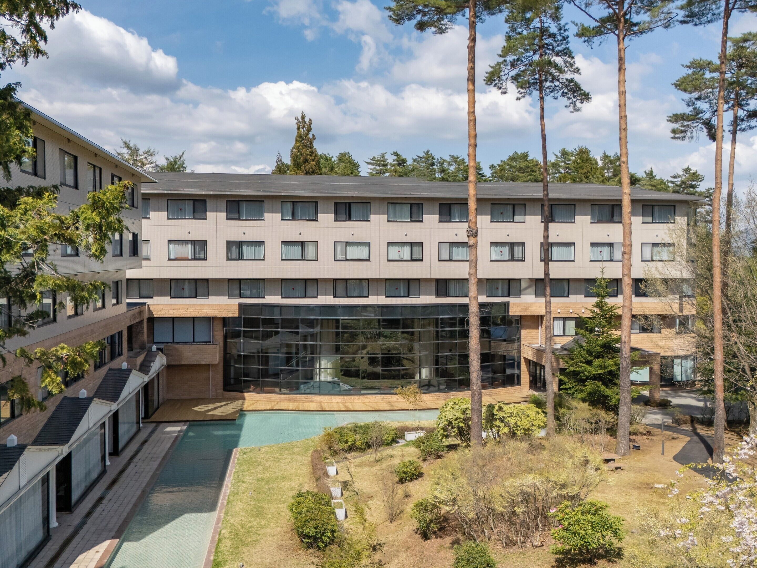 Un hotel de varios pisos con un patio central, piscina y una amplia fachada de vidrio.