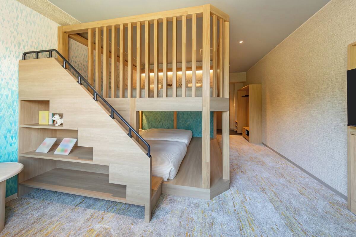 A multi-level room with a wooden staircase, bunk beds, a desk, and a television.
