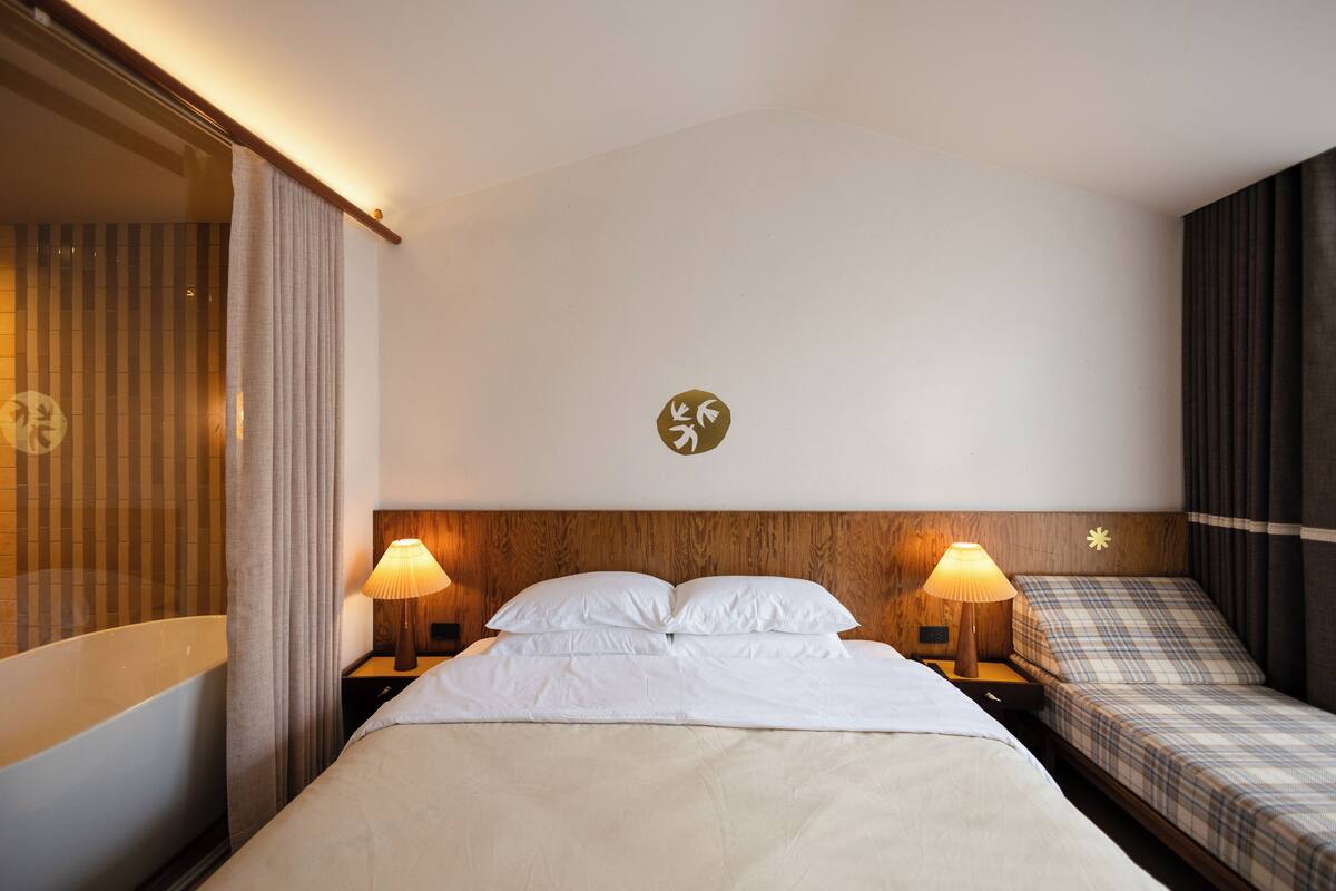 Habitación de hotel con una cama grande, dos mesitas de noche con lámparas, un cabecero de madera y una lámpara fijada a la pared.