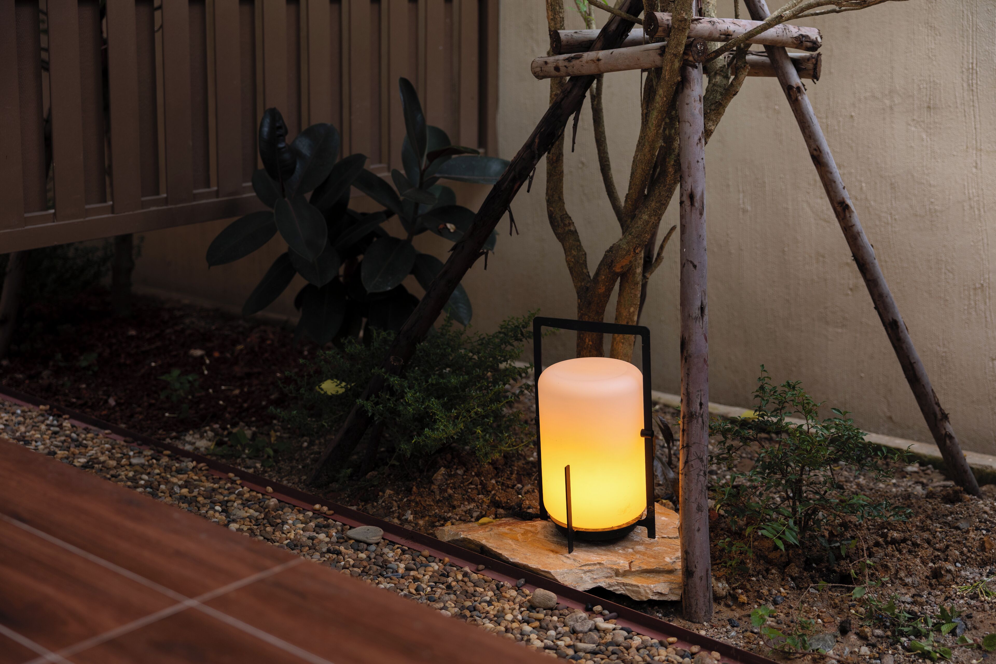 A lantern-style light fixture mounted on a wooden stand in a garden setting.