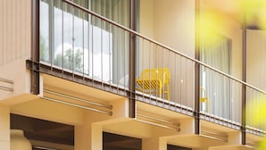 Un edificio moderno con balcón, barandillas y una silla amarilla.