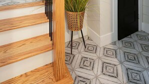 Uma escadaria com degraus de madeira e guarda-corpos pretos, um vaso de planta e um piso com padrão.