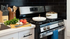 Cozinha com painel de azulejos pretos, fogão de aço inoxidável e exaustor de madeira sobre o fogão.
