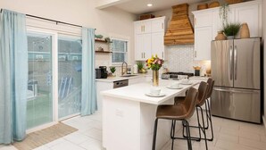 A modern kitchen with white cabinetry, a stainless steel refrigerator, and a central island with bar stools. - 2x Home Entertainment Oasis. Sauna, Hot Tub, Games (Galveston)