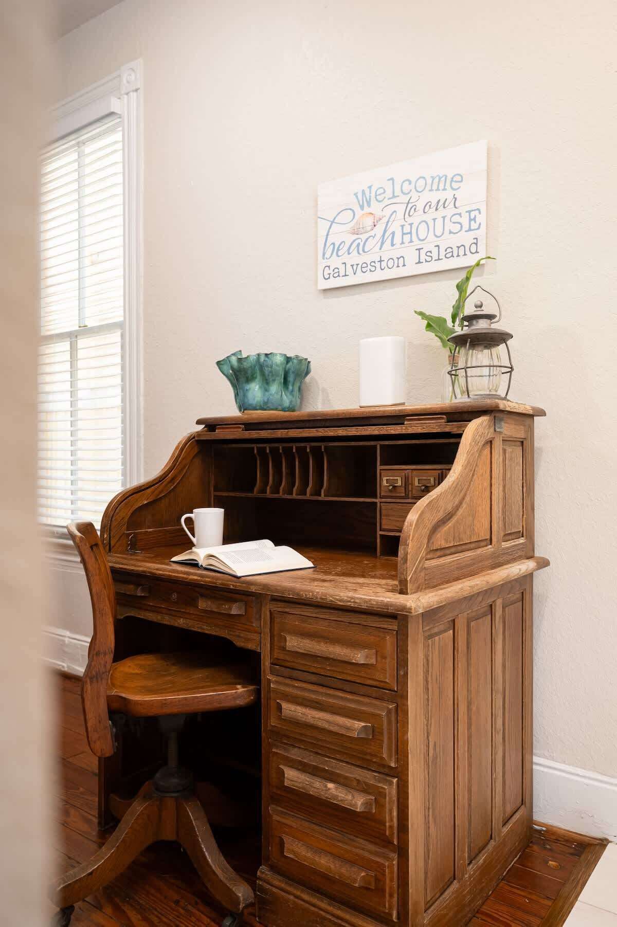 A wooden desk with a cup and book, a sign reading "Welcome to our beach house Galveston Island", and a lantern on the wall.