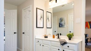 A bathroom with a white vanity, a large mirror, and a framed abstract painting on the wall. - Modern Entertainer's Dream: Pool | Cabana | Games (Humble)