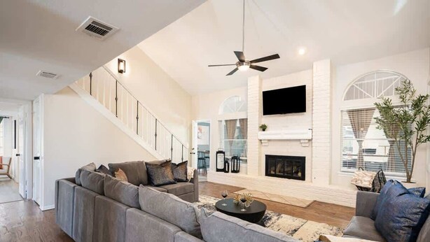 A spacious living room with a large gray sectional sofa, a fireplace, and a staircase leading to an upper level. - Modern Entertainer's Dream: Pool | Cabana | Games (Humble)