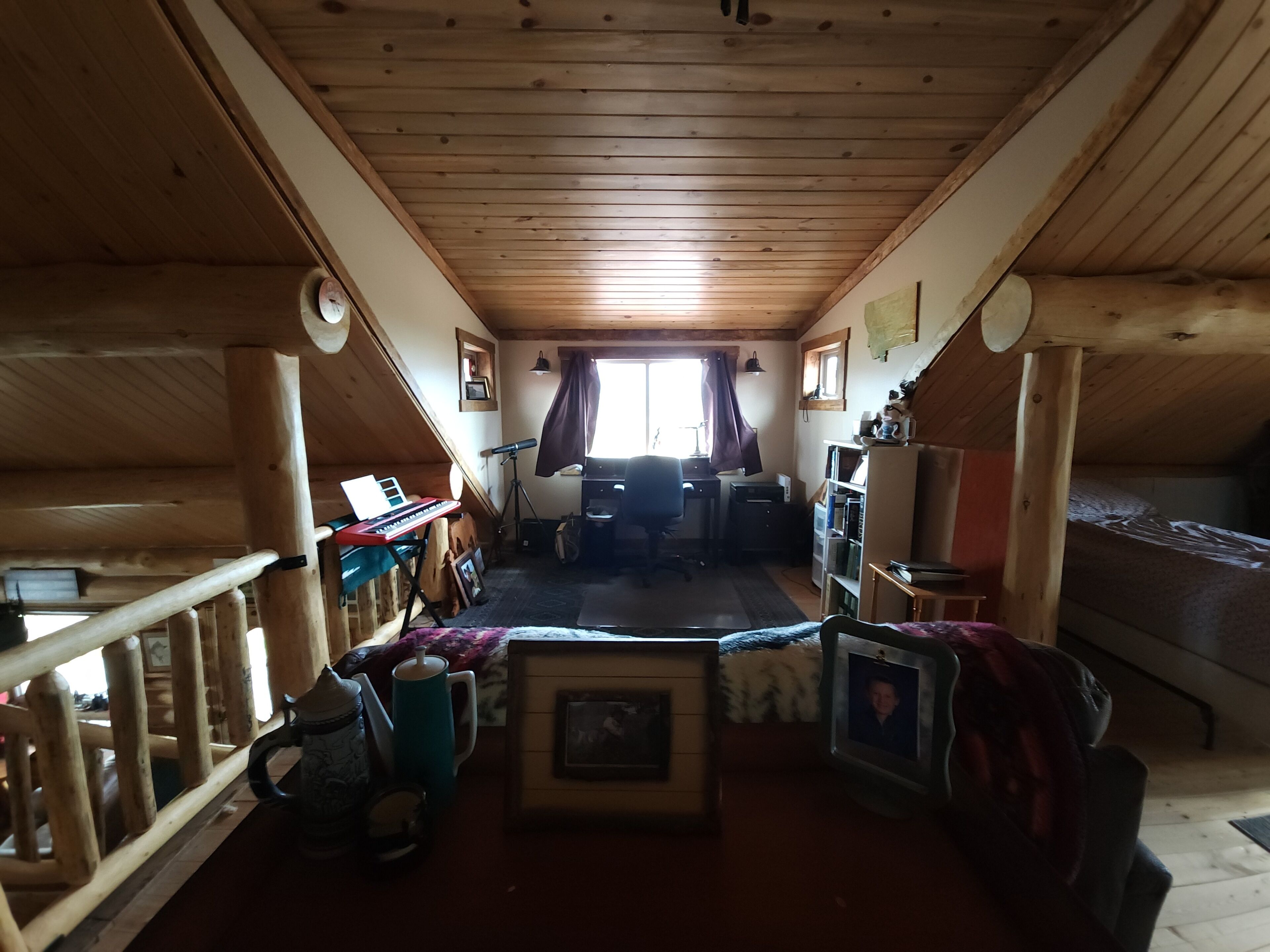 Une pièce mansardée chaleureuse avec des poutres en bois, un bureau, une chaise, un lit et une fenêtre avec des rideaux.