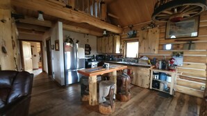 A rustic cabin interior with a wooden dining table, a refrigerator, and a kitchen area. - Charming 2-bedroom cabin in Emigrant with Beautiful Views (Emigrant)