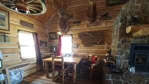 A rustic cabin interior with a wooden dining table, chairs, a stone fireplace, and mounted animal heads on the walls. - Charming 2-bedroom cabin in Emigrant with Beautiful Views (Emigrant)
