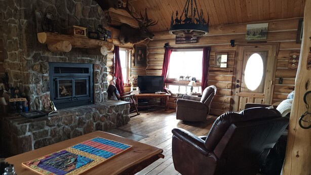 A cozy log cabin interior with a stone fireplace, a television, leather seating, and a chandelier. - Charming 2-bedroom cabin in Emigrant with Beautiful Views (Emigrant)