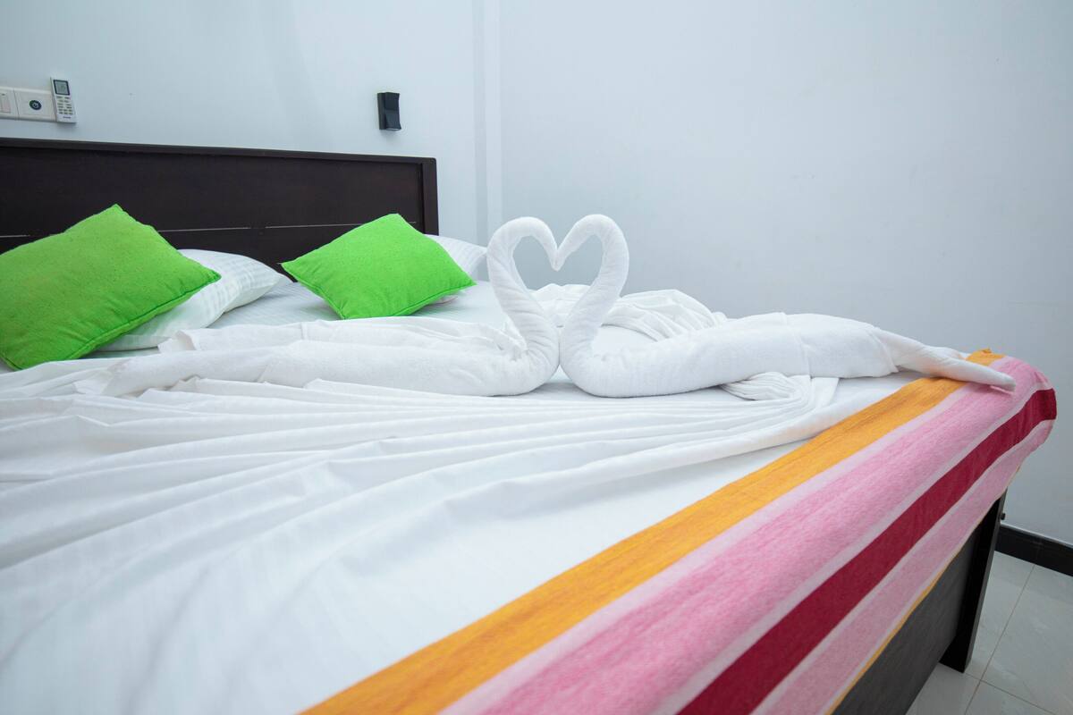 A hotel room with a neatly made bed, green pillows, and a striped bedspread.