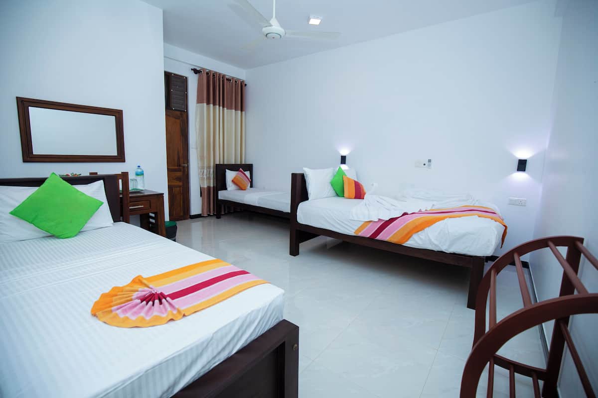 A hotel room with two beds, a chair, a desk, a mirror, and a ceiling fan.
