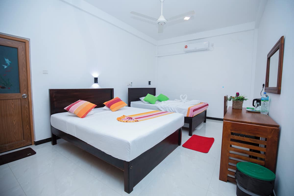 A hotel room with a bed, bedside tables, a desk, a trash bin, a red rug, and a ceiling fan.