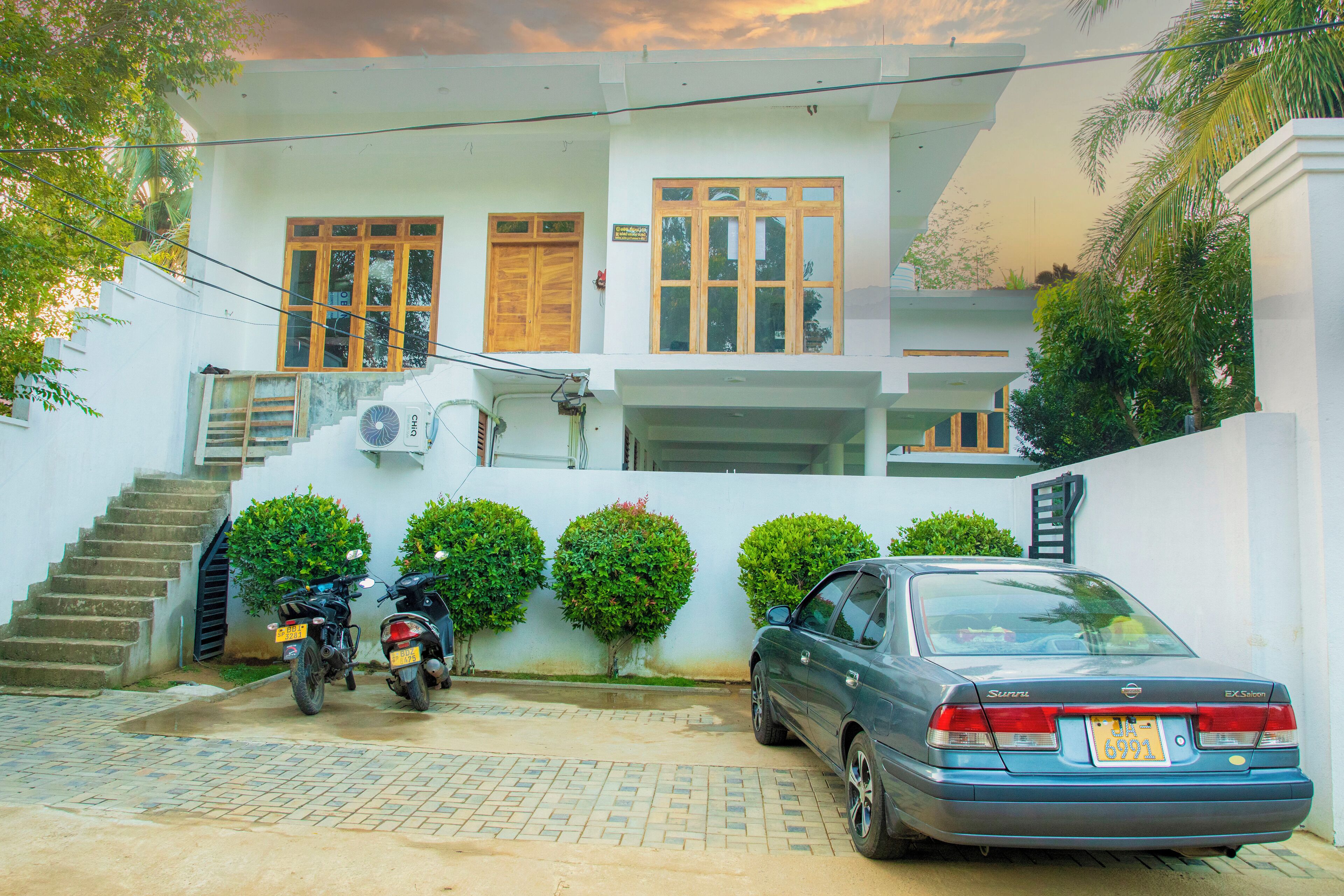 A two-story building with a staircase leading to the upper floor, a parked car, and two motorcycles.