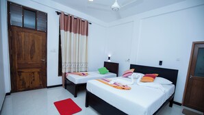Een hotelkamer met twee bedden, een houten deur, een rode mat en een plafondventilator.