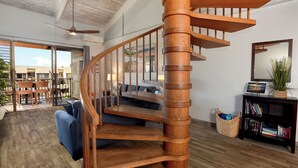 Una escalera de caracol de madera en un salón moderno con un ventanal grande, un sofá azul y una estantería.