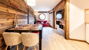 A dining area with a wooden wall, a red sofa, and a round window.