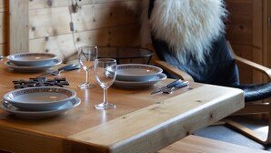 Un intérieur en bois avec une table à manger dressée pour deux personnes, un téléviseur fixé au mur et un plaid en fourrure sur la chaise.