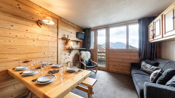 Une pièce chaleureuse aux murs en bois, une table à manger dressée avec des assiettes et des verres, un fauteuil rembourré et un canapé.