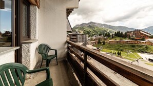 Un balcon donnant sur un village de montagne, avec des balustrades en bois et une chaise verte.