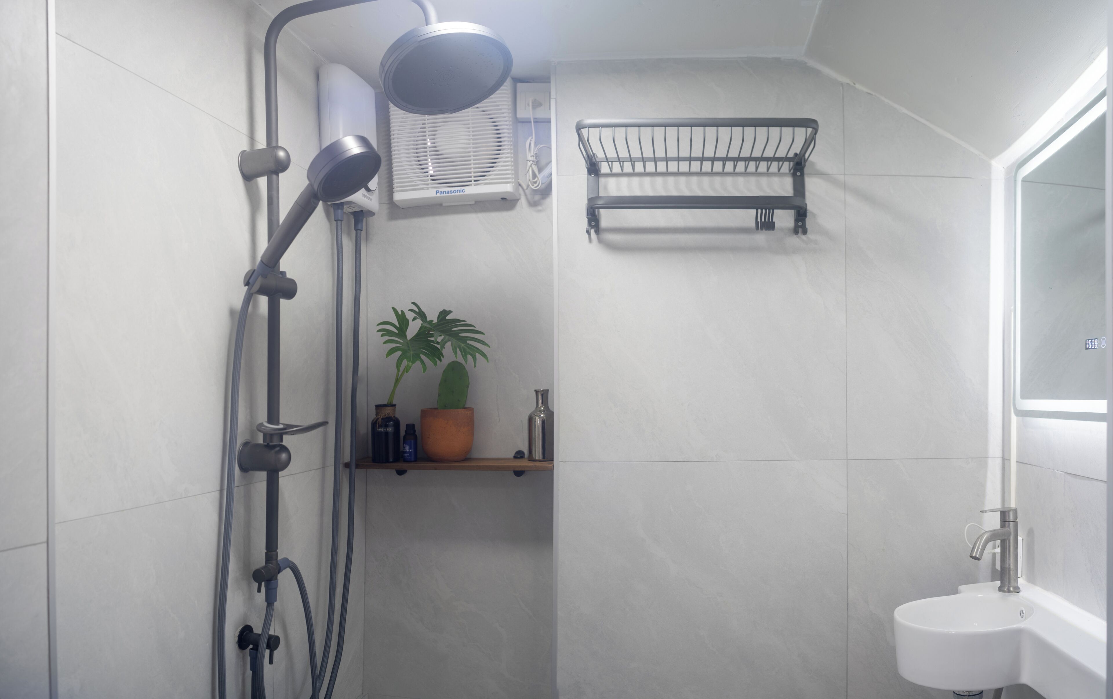 A modern bathroom with a shower, a sink, and a shelf with a plant and toiletries.