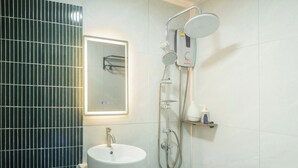 Ein Badezimmer mit einem weißen Waschbecken, einem Spiegel, einer Dusche mit Duschbrause und einem Ablagebereich für Toilettenartikel.