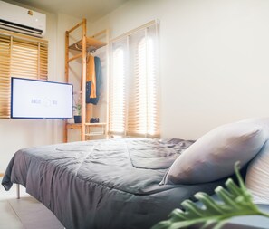 Un dormitorio con cama, televisión, escalera de madera y ventana con persianas.