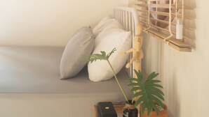 Ein kleiner, gemütlicher Raum mit einem Bett, einem Nachttisch aus Holz, einer Topfpflanze und einem Fenster mit Holzjalousien.