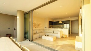 A modern living room with a large sectional sofa, a coffee table, and a glass door leading to a kitchen area.