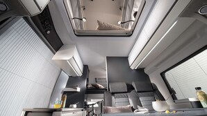 A modern train compartment with a bunk bed, a small kitchenette, and a seating area with a table and chairs.