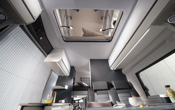 A modern train compartment with a bunk bed, a small kitchenette, and a seating area with a table and chairs.