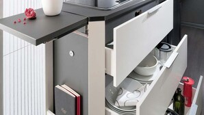 A modern kitchen with a built-in stove, a pomegranate on the counter, and a book in a drawer.