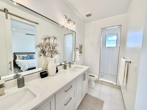 Une salle de bain moderne avec deux lavabos, un grand miroir, une cabine de douche et des toilettes.