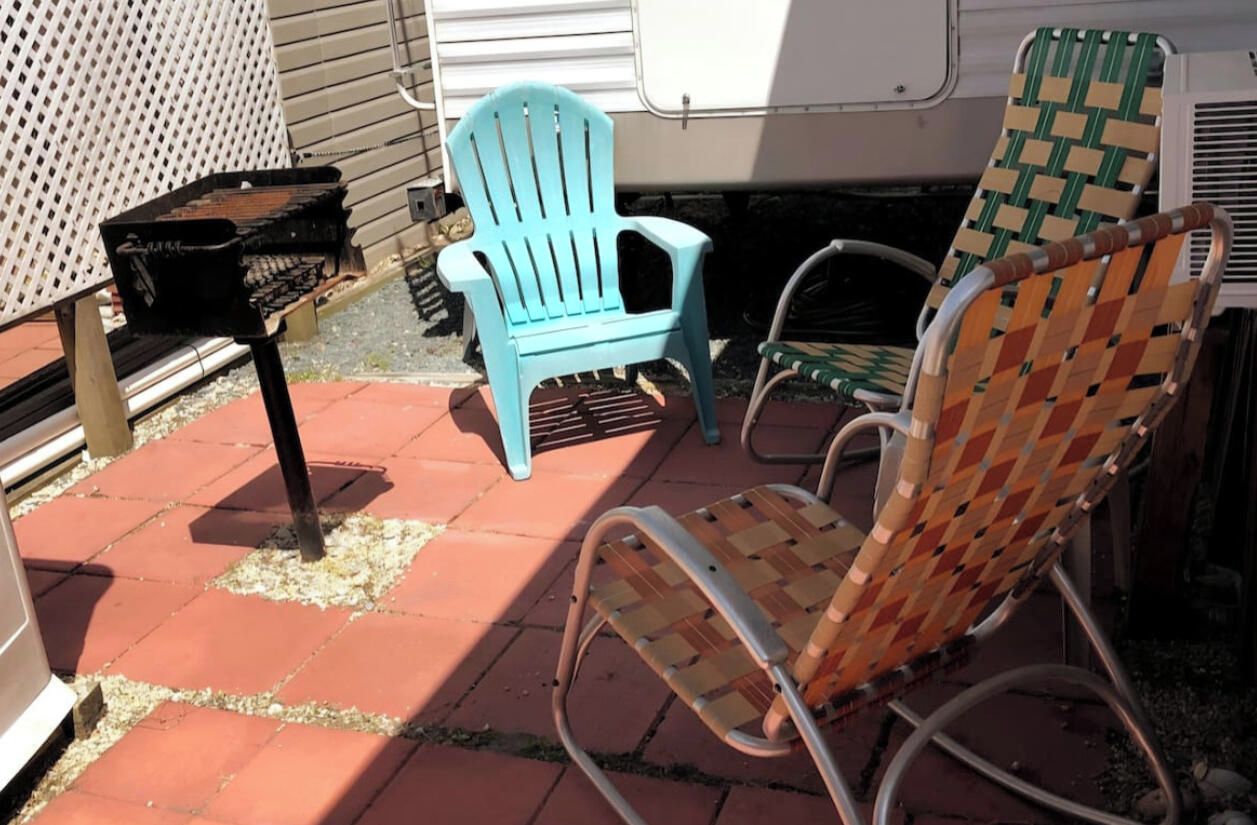 Une terrasse aménagée avec du mobilier d’extérieur, notamment un fauteuil Adirondack bleu et un fauteuil en osier.
