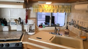A compact kitchen with a stove, sink, and coffee maker. - Cozy Camper North Topsail Beach (North Topsail Beach)