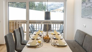 A dining area with a large table set for six, chairs, a sofa, and a view of a snowy landscape through large windows. - Alpine Qualitytime by Interhome (Wildschönau)
