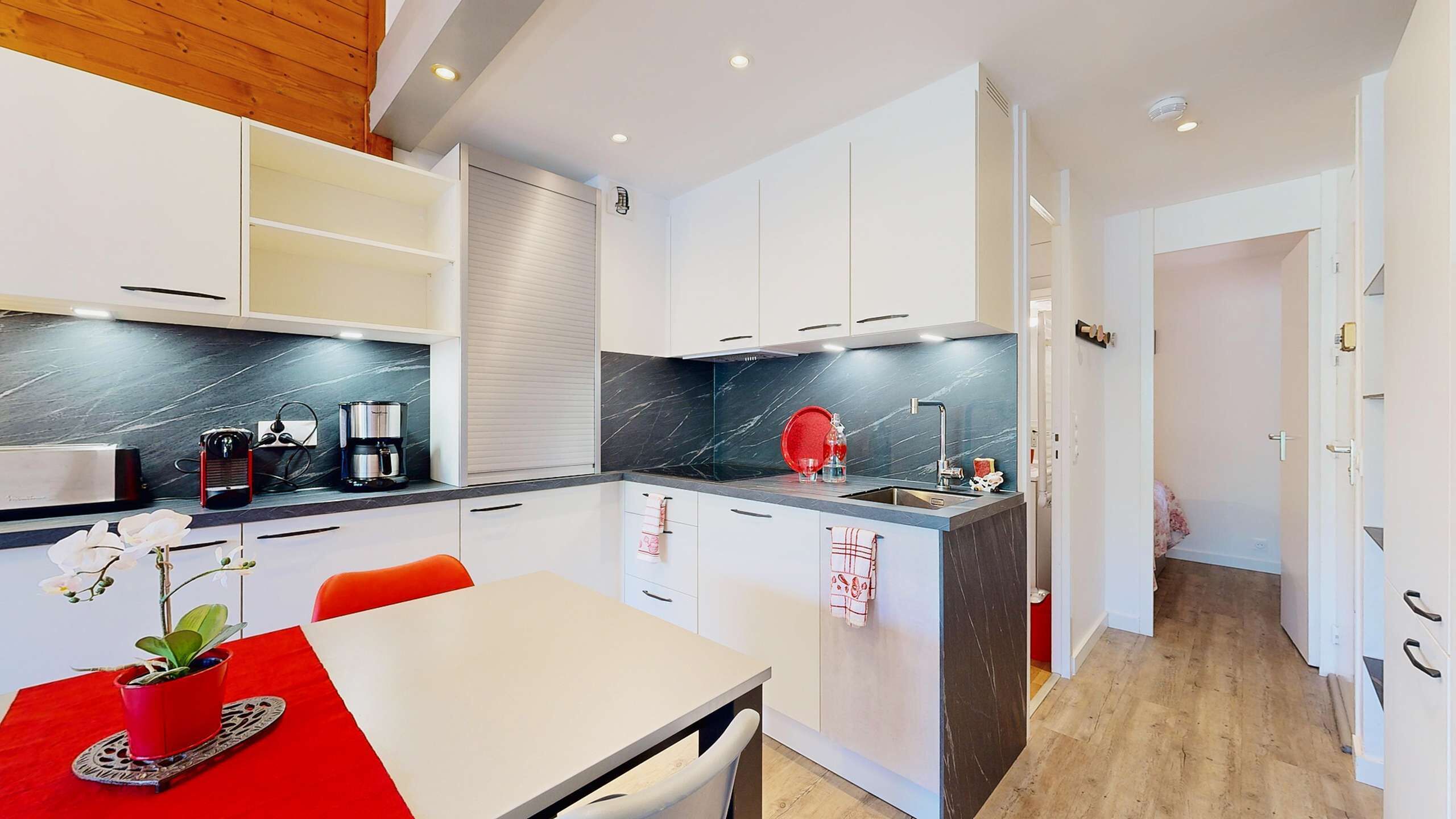 A modern kitchen with white cabinets, a black marble countertop, and a red accent wall.