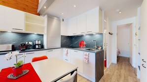 A modern kitchen with white cabinets, a black marble countertop, and a red accent wall. - Cheval Blanc 32 - Crève Coeur (LES AVANCHERS VALMOREL)