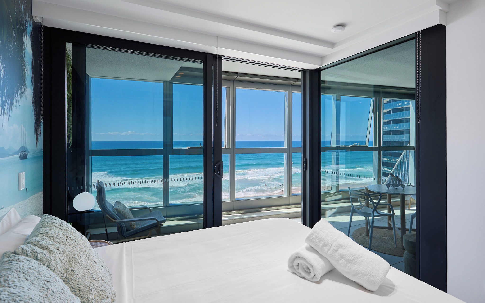 Habitación de hotel con un amplio ventanal corredera que da a un balcón con vistas al océano y un puente.