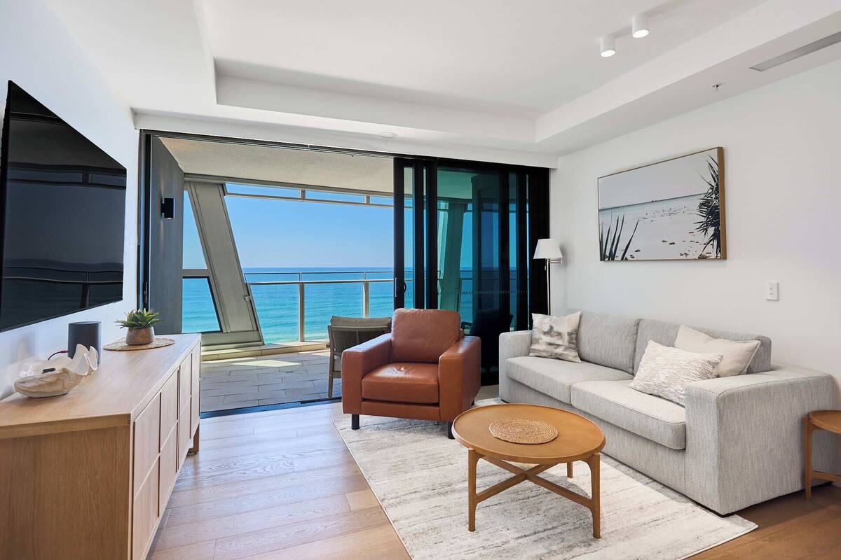 Un moderno salón con sofá, sillón y mesa de centro, una televisión y vistas al mar.