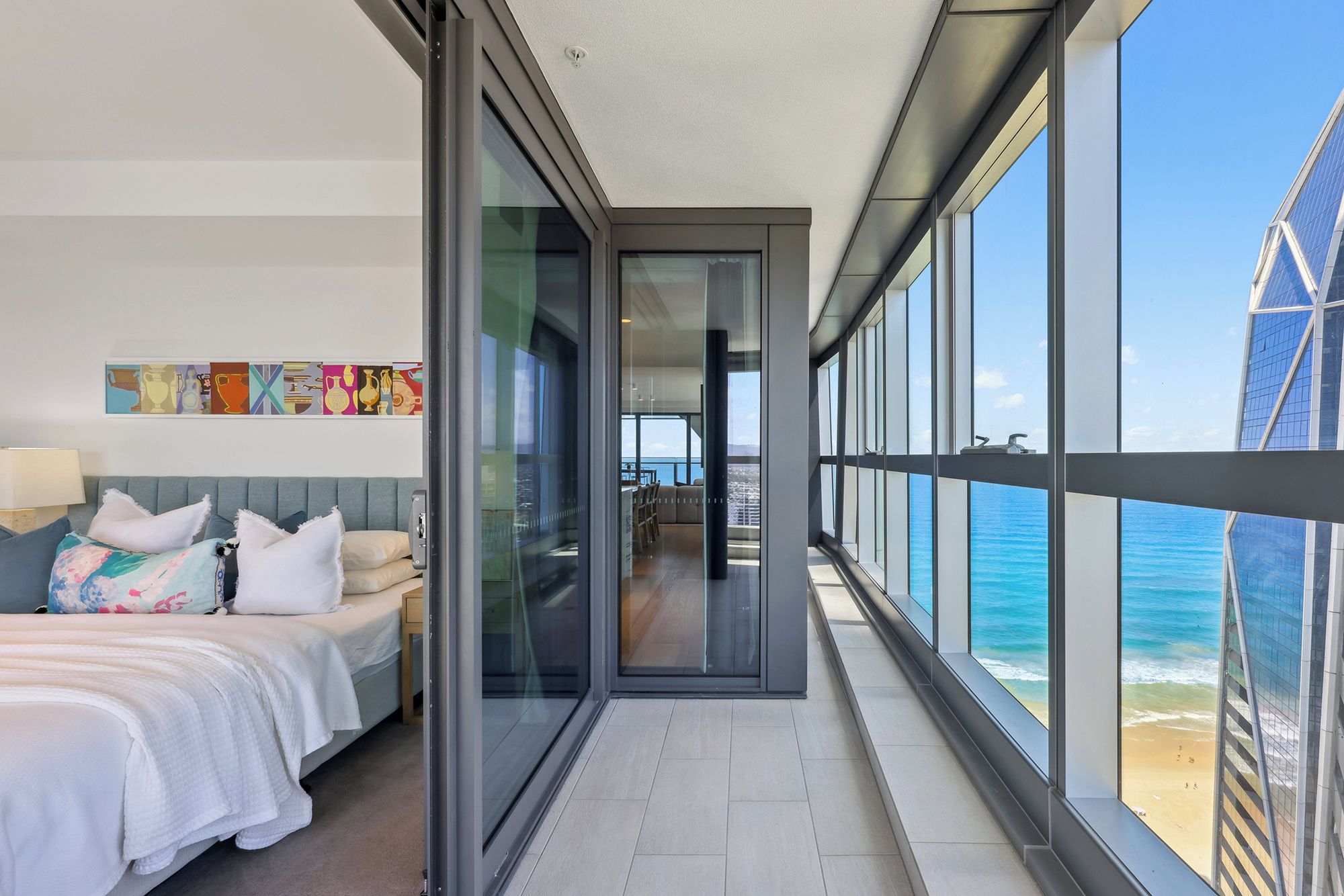 A modern hotel room with a bed, a desk, and a view of the ocean through large windows.