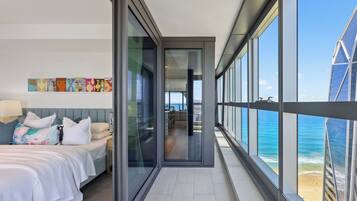 A modern hotel room with a bed, a desk, and a view of the ocean through large windows.